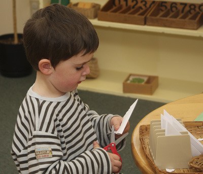 A four-year-old at Orcas Montessori School concentrates on cutting paper for an artistic activity.