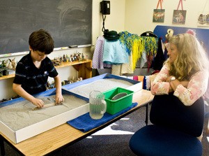 Margie Sabine looks on as Eddie Cunningham plays with the sand tray in the Primary Intervention Project playroom.