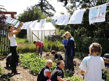 F2C Garden Keeper Chelsea Cates hangs flags for Farm to Classroom kids while they harvest some radishes from the garden.