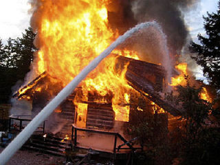 Water from a “Fire Cannon” mounted atop an Orcas Island Fire Department engine hits the flaming cabin.