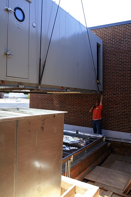 A University Mechanical employee helps position the HVAC system in place